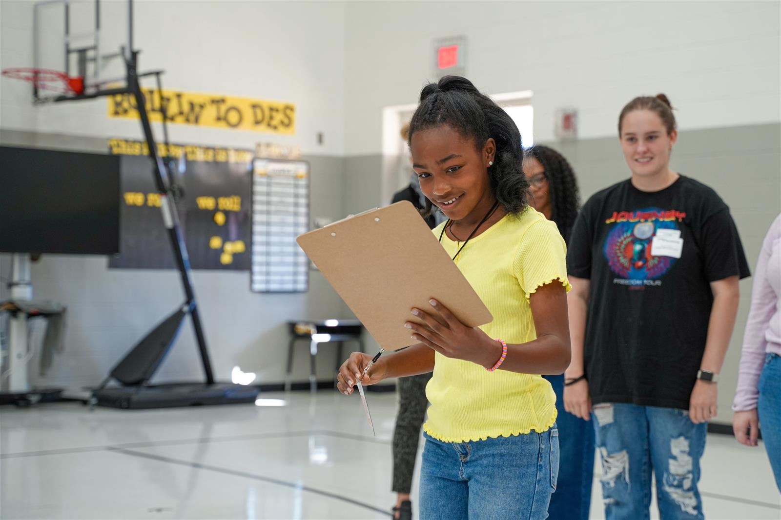 young girl in a yellow shirt holds a clip board